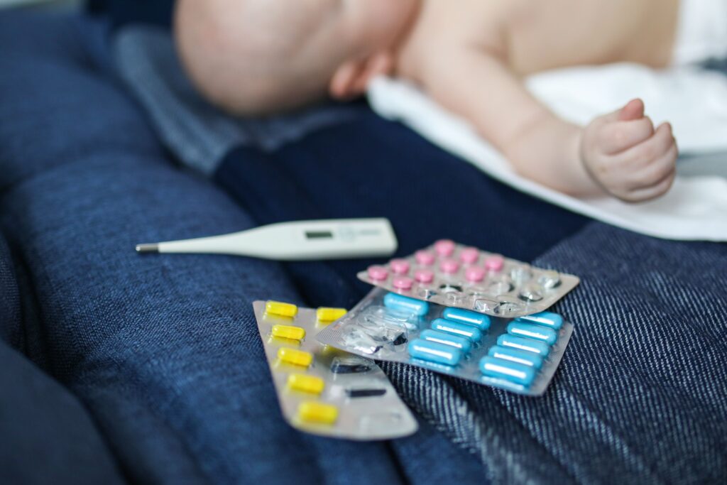 감기약, 빈속에 먹어도 될까? 공복 복용 시 주의해야 할 약들. A baby lying next to various medications and a thermometer, suggesting health issues.